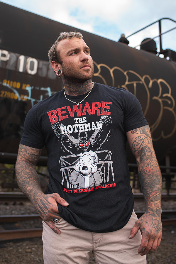 Man wearing a black t-shirt with graphic design and text, standing in front of a train.
