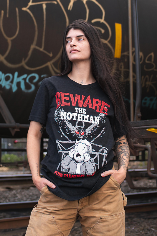 Person wearing a black t-shirt with graphic design and text, standing against a graffiti-covered wall.