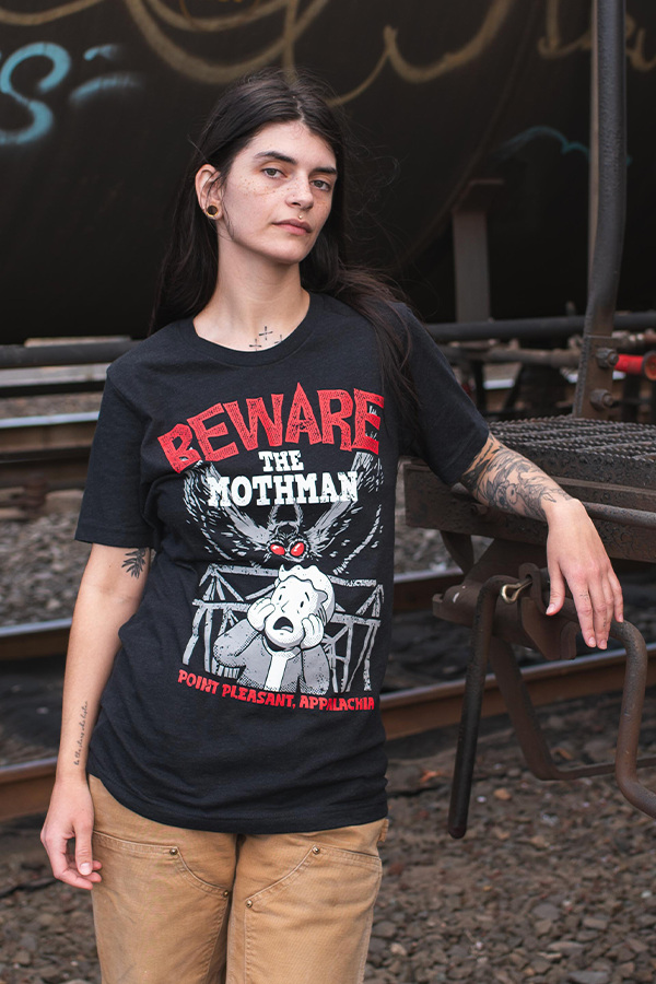 Person wearing a black t-shirt with a graphic design and text, standing on train tracks.