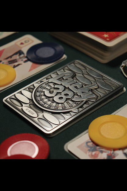 Top-down shot of the back of the Lucky 38 metal Ace of Spades, with the metal poker chip and metal pin badge among playing cards and chips.