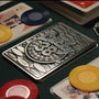 Top-down shot of the back of the Lucky 38 metal Ace of Spades, with the metal poker chip and metal pin badge among playing cards and chips.