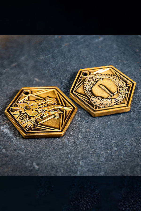 The hexagonal metal D2 coin with its antique gold plating. It is embossed on both sides: one with the Ebonheart Pact’s Dragon head, the other with the game’s three-headed Ouroboros.