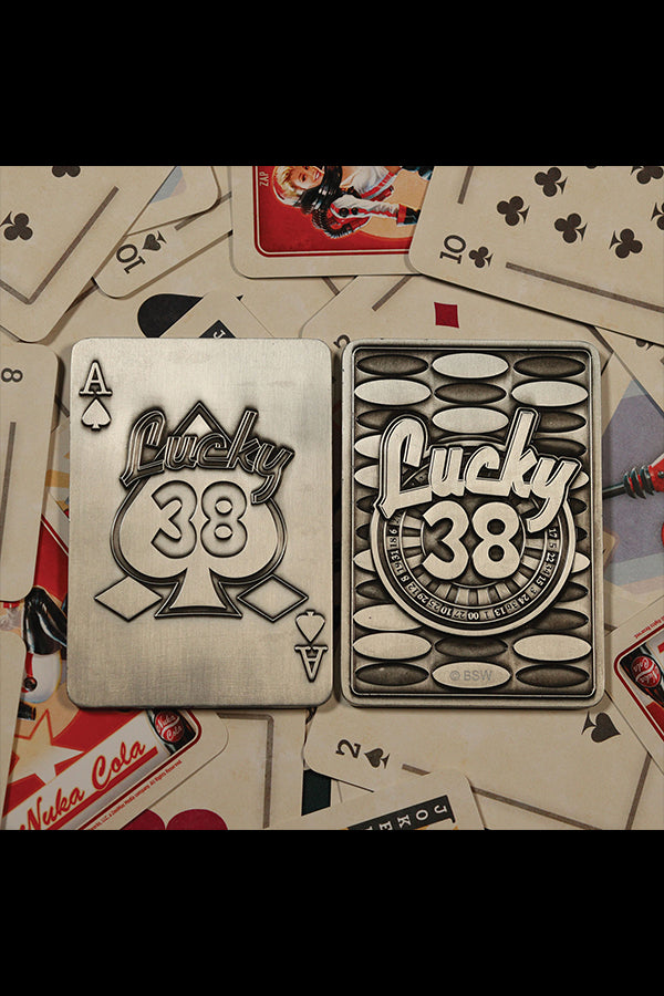 Top-down shot of the back of the Lucky 38 metal Ace of Spades, with the metal poker chip and metal pin badge among playing cards and chips.