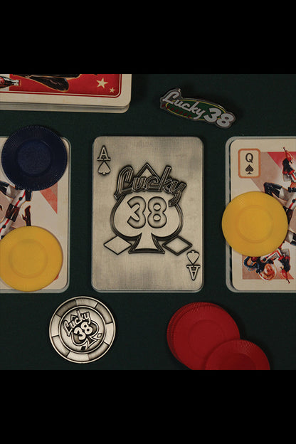 Top-down shot of the back of the Lucky 38 metal Ace of Spades, with the metal poker chip and metal pin badge among playing cards and chips.